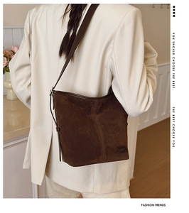 Détail d'un sac seau en daim marron foncé porté avec un blazer blanc surdimensionné