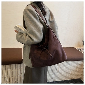 Detail of a brown suede tote bag with drawstring texture shown on a model's shoulder