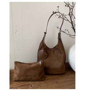 Detailed close-up of brown frosted suede hobo bag with matching zipper pouch on wood