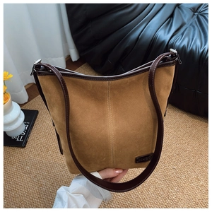 Détail d'un sac seau en daim marron avec garniture en cuir et logo sur un tapis douillet