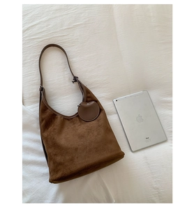 Deep brown suede hobo bag with leather strap and round charm shown next to an iPad for scale