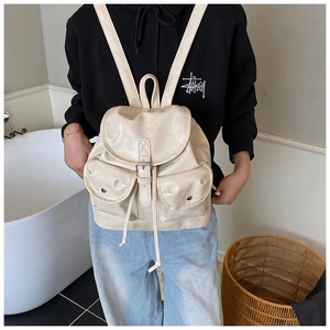Detail view of a cream vintage backpack with flap closure and decorative buckles on a model