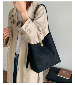 Detail of black suede bucket bag featuring golden twist lock with chic beige trench coat