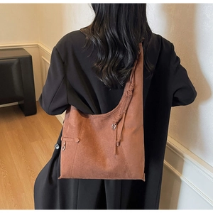 Detail of reddish-brown suede tote bag with decorative knot and silver metal ring