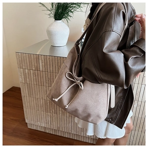 Detail of brown suede tote bag featuring a cream drawstring bow and textured finish