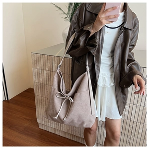 Detail of beige suede tote bag featuring side pockets and a delicate bow decoration
