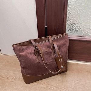 Close-up of burgundy suede tote bag with brown leather trim and fashion tag detail