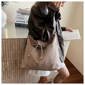 Detail of taupe suede tote bag with drawstring bow on a model in a minimalist setting