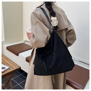 Detail of black suede tote bag featuring a decorative drawstring bow and wide shoulder strap