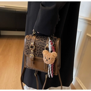 Detail of leopard print backpack with brown leather trim and plush bear charm