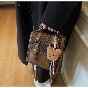 Detail of leopard print backpack with brown plush bear charm and buckle flap closure