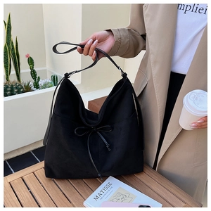 Detail of a large black suede tote bag with a decorative drawstring bow and wide strap