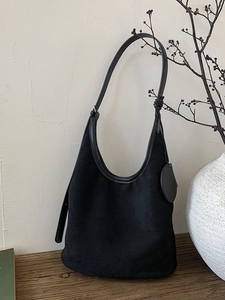 Large black suede hobo shoulder bag on a wooden table with minimalist decor