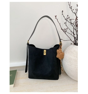 Detail view of black suede bucket bag with gold square buckle and brown teddy charm