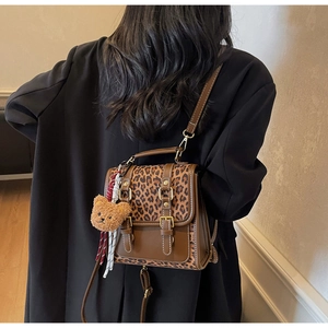 Detail of leopard print backpack featuring a brown plush bear charm and golden hardware