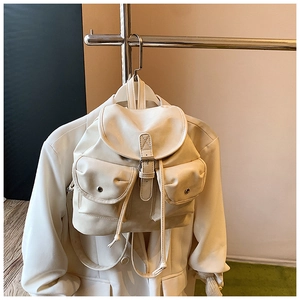 Detail of the cream-colored faux leather backpack featuring a top flap and magnetic buckles