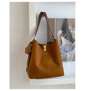 Detail of vintage brown suede shoulder bag featuring a gold clasp and a pompom charm