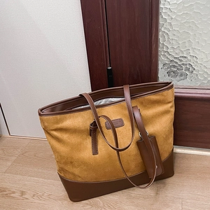 Close-up of mustard suede tote bag with brown faux leather trim and brand plate detail