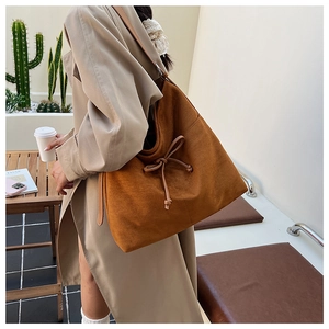 Brown suede tote bag with ribbon bow detail styled over a beige trench coat