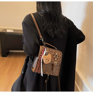 Detail of leopard print backpack with brown leather, gold buckle and bear charm decor
