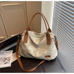 Close-up of light green canvas tote bag with brown woven handles and leather logo tag