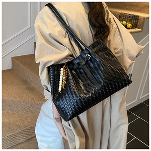 Detail of black woven leather tote bag featuring vintage V-pattern and wooden bead charm