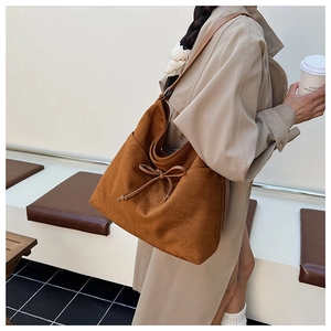 Detail view of large caramel suede tote bag with bow accent on a trench coat model