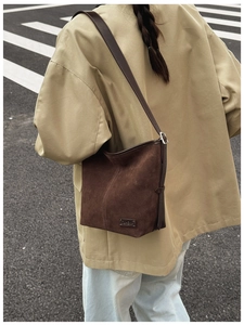 Détail du sac seau en daim marron mat avec logo métallique et bandoulière réglable