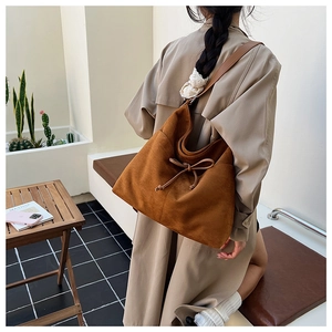 Detail of caramel suede tote bag featuring a leather drawstring bow and wide shoulder strap