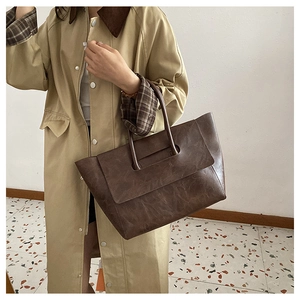 Detail view of large dark brown retro leather tote bag held by model wearing a trench coat