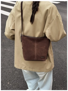 Sac seau en daim marron porté en bandoulière sur un trench-coat classique en extérieur