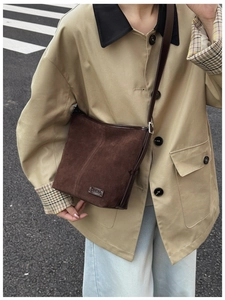 Gros plan sur un sac seau en daim marron orné d'une plaque de marque CAHEKA en métal poli