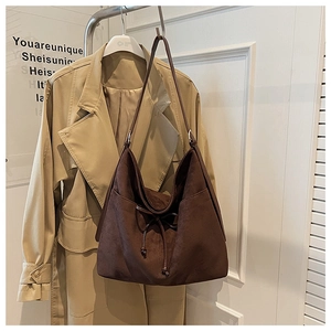 Brown suede hobo bag with drawstring bow detail hanging next to a khaki trench coat