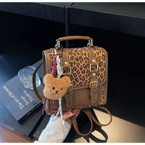 Detail of leopard print patchwork backpack featuring leather straps and a plush bear charm
