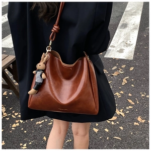 Detail of brown leather hobo bag with a plush bunny charm and decorative strap knots