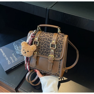Detail of leopard print backpack with brown leather straps and cute plush bear charm