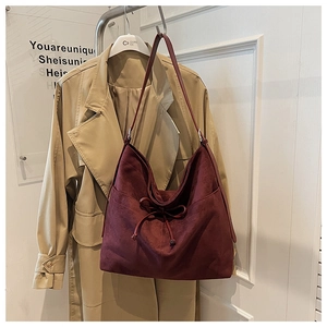 Detail of burgundy suede tote bag featuring decorative bow tie and vertical stitching