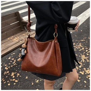 Close-up of brown leather tote bag with a cute rabbit charm in an autumn street setting