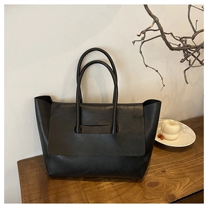 Detail view of a black vintage tote bag with a unique flap design on a wooden surface