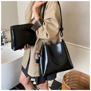 Close-up of black glossy tote bag with metal rings and rabbit charm on person