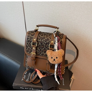 Detail of leopard print backpack with brown leather trim and cute plush bear charm