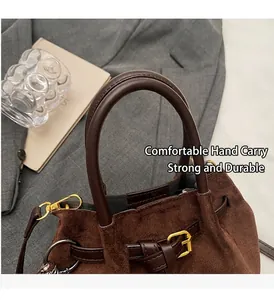 Detalle del bolso de ante marrón oscuro con asas de cuero liso y hebillas doradas de metal
