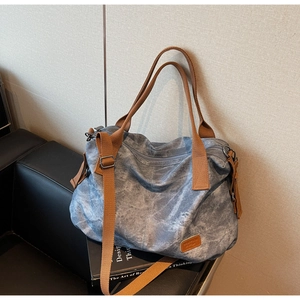 Detail of vintage blue canvas tote with adjustable brown strap on a leather sofa