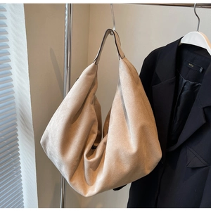 Détail du sac hobo en daim beige mat suspendu à côté d'un blazer pour l'échelle