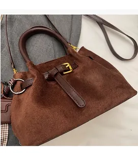 Detalle del bolso tipo cubo en ante marrón oscuro con correas de cuero y hebilla dorada