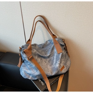 Detail of grey-blue canvas tote bag featuring side zipper pocket and brown shoulder strap