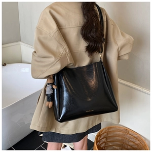 Detail of black faux leather tote bag with glossy texture and cute brown bear pendant charm