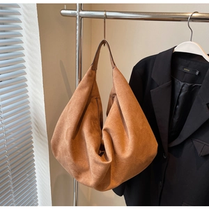 Détail du sac hobo en daim caramel avec une large bandoulière dans un décor élégant