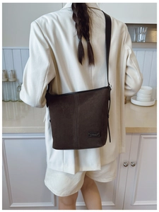 Détail du sac seau en daim mat avec bandoulière réglable sur fond clair neutre