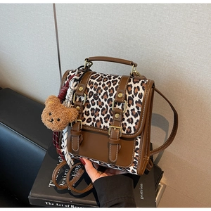 Detail of leopard print backpack with brown leather trim, metal buckle and plush bear charm